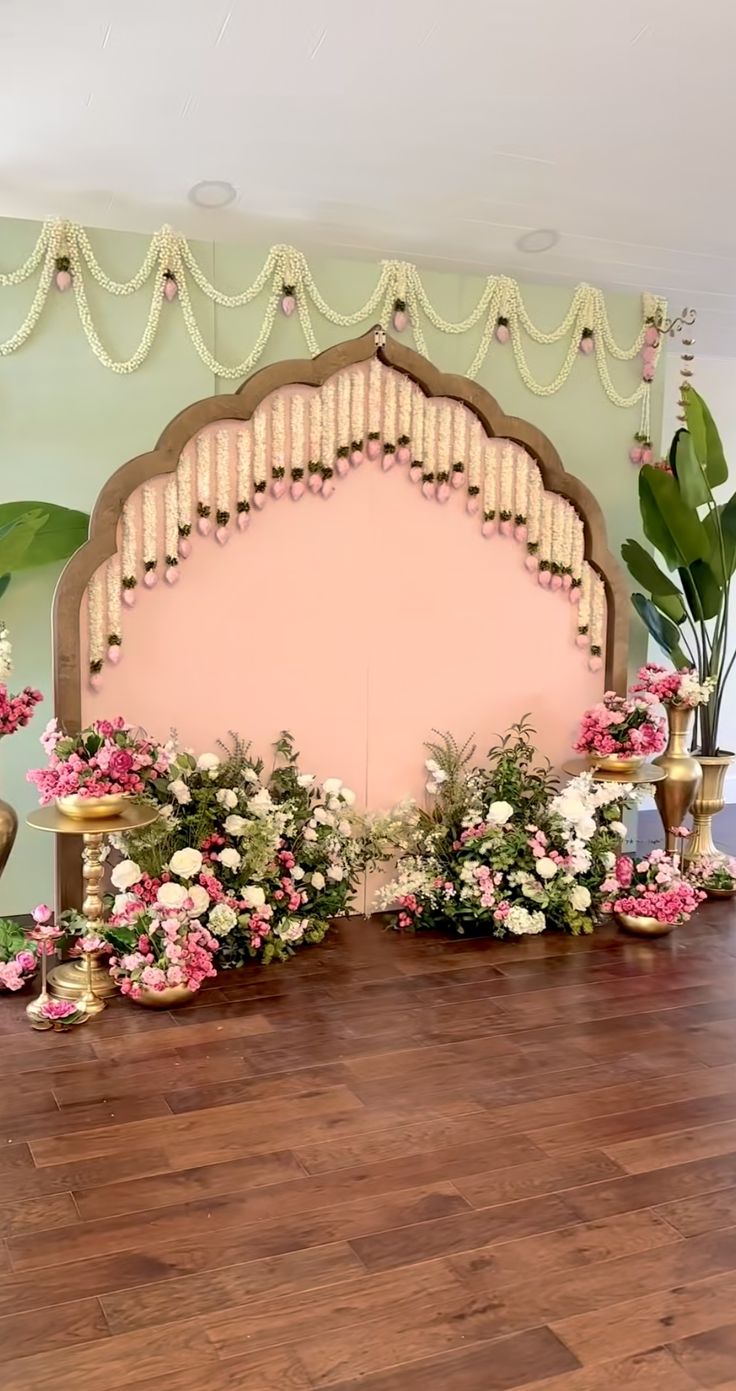 a room decorated with pink and white flowers, gold vases and greenery on the floor