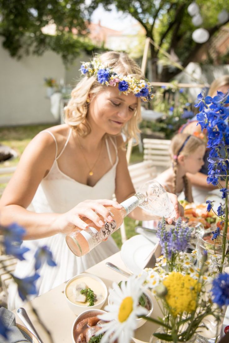 a woman in a white dress pouring water at a table with blue and yellow flowers