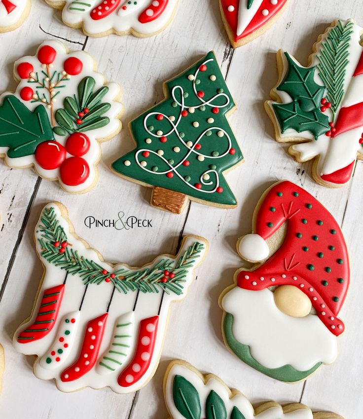 decorated christmas cookies on a white wooden surface with holly, stockings, and tree decorations