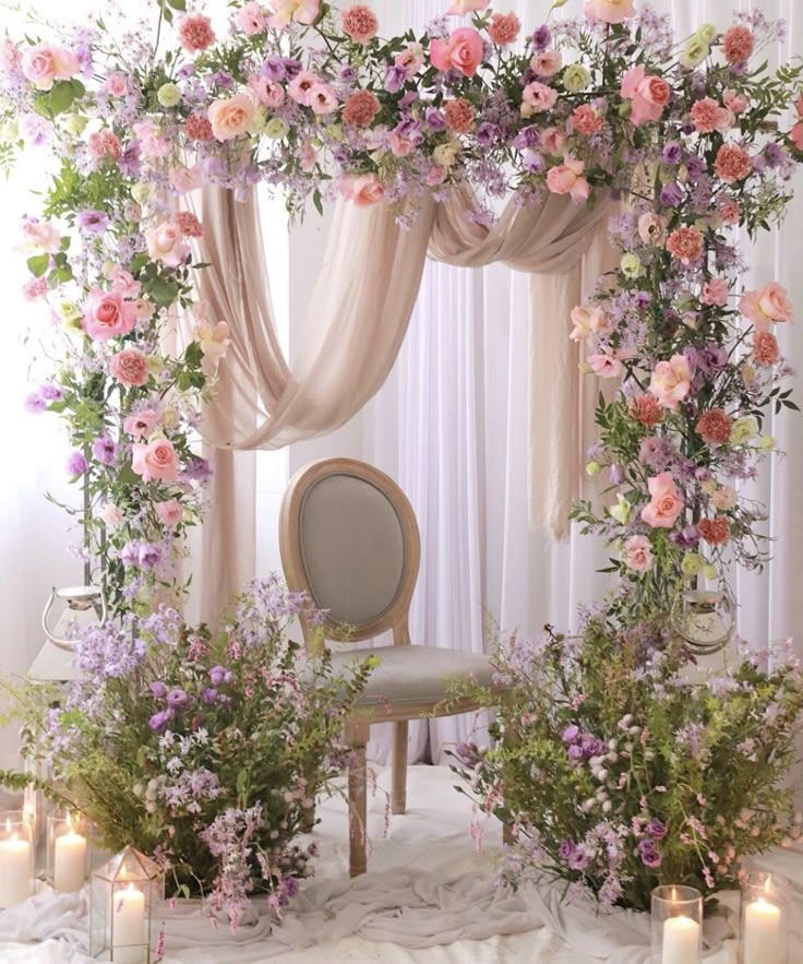 a chair sitting in front of a flower covered stage with candles and flowers around it