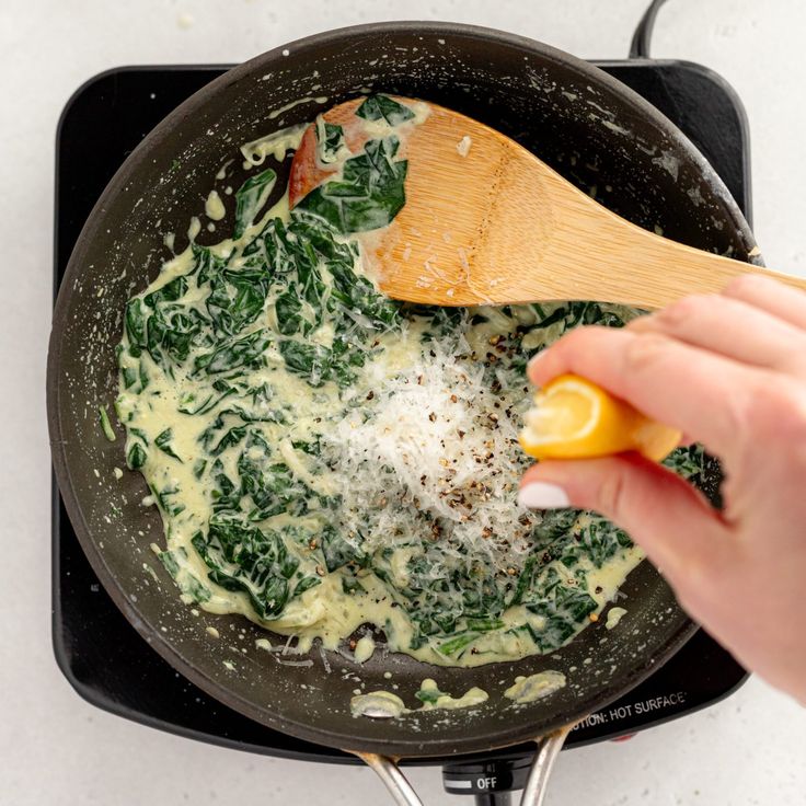 someone is cooking spinach and cheese in a skillet with a wooden spoon on the stove