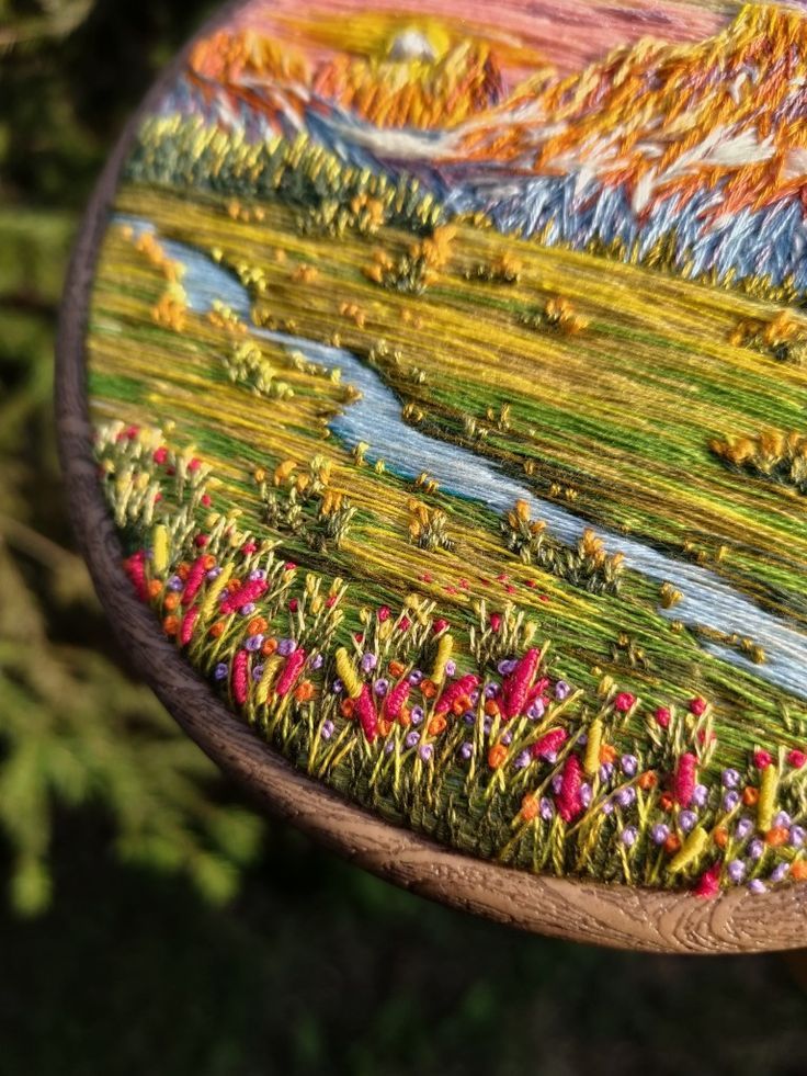 a wooden table topped with a painting on top of a forest covered in flowers and grass