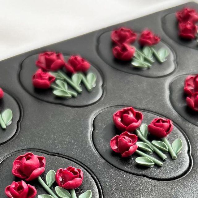 cupcakes decorated with red tulips and leaves in a muffin tin