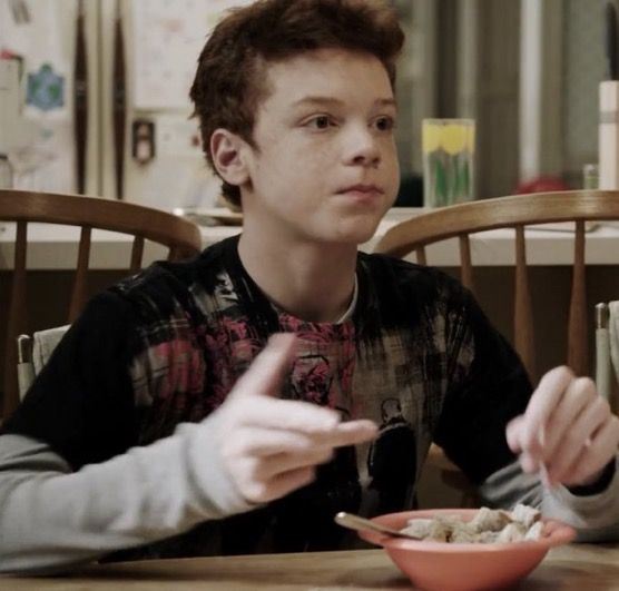 a young boy eating cereal from a bowl on top of a wooden dining room table