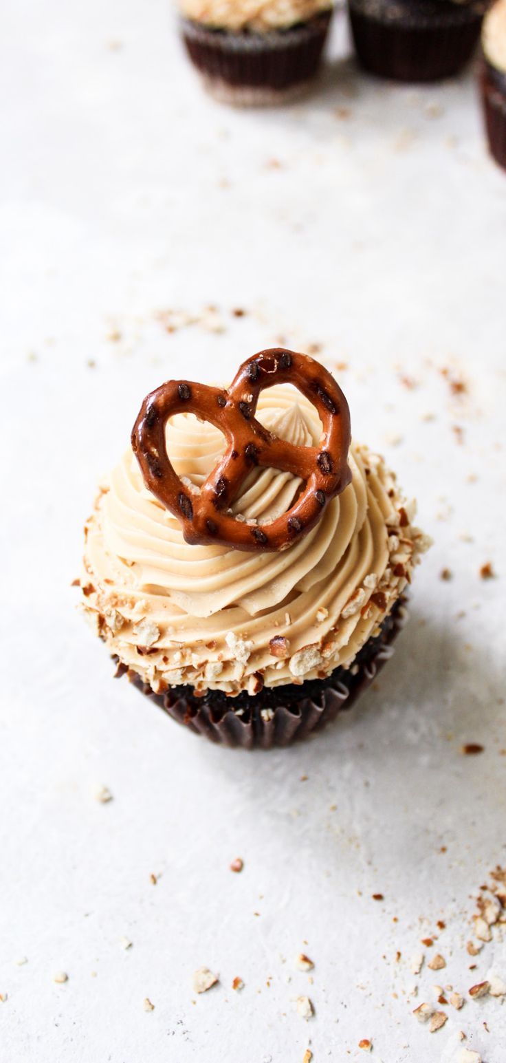 some cupcakes with frosting and pretzels on top are sitting on a table