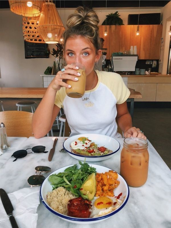 a woman sitting at a table with plates of food and drinks in front of her