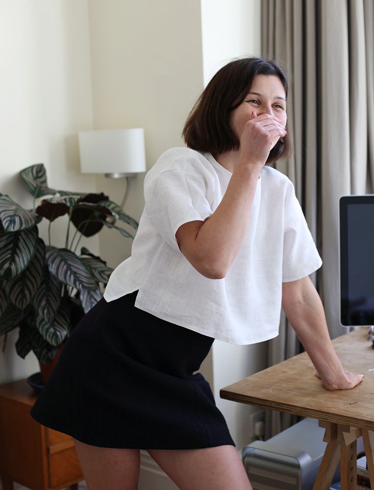 a woman standing in front of a computer desk with her hand on her mouth and looking at the screen