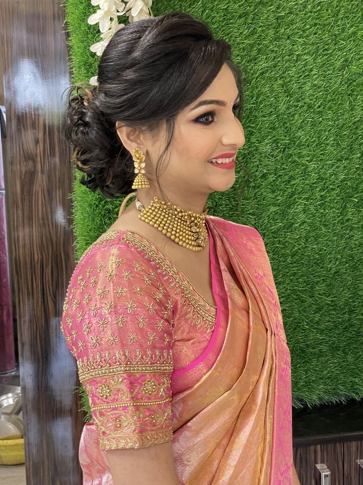 a woman in a pink and gold sari standing next to a wall with grass behind her