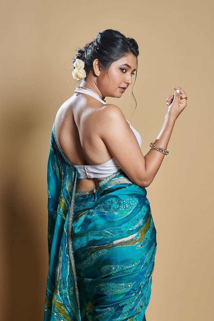 a woman in a blue sari is holding her hand up to the side and looking down