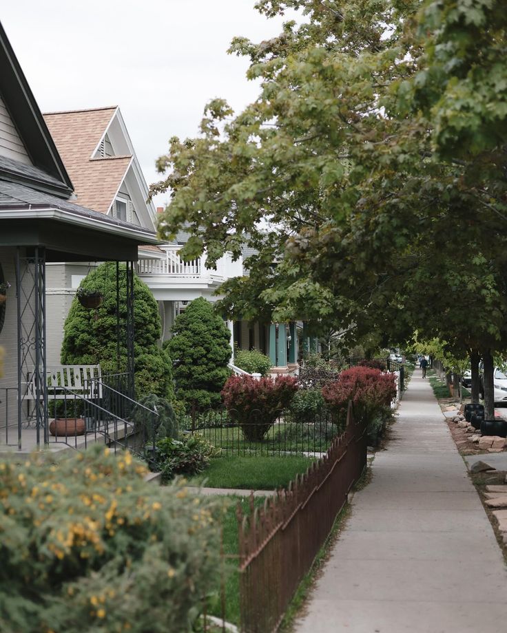 the sidewalk is lined with flowers and trees in front of some houses on a cloudy day