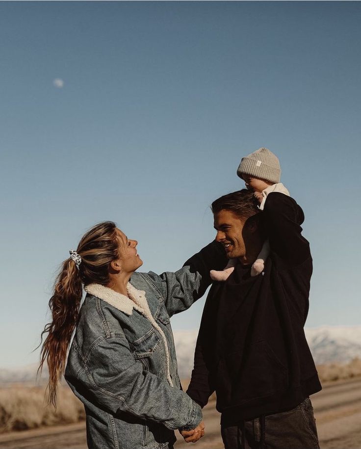 a man and woman holding a baby on their shoulders in the middle of an empty road