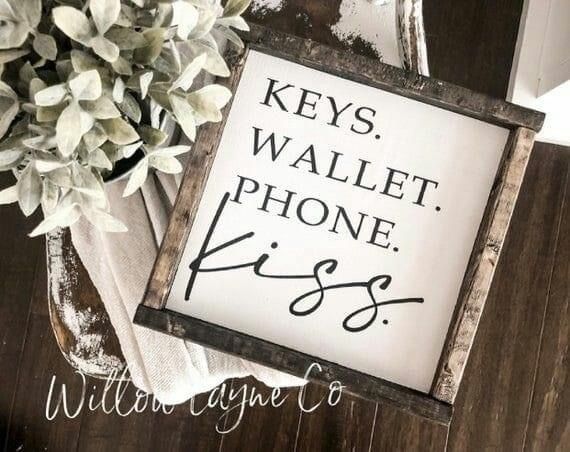 a sign that says keys wallet phone kiss on it next to a potted plant