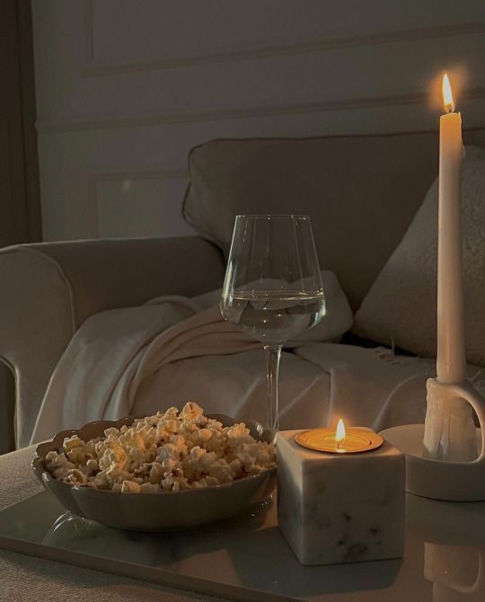 a glass of wine and bowl of food on a tray next to a lit candle