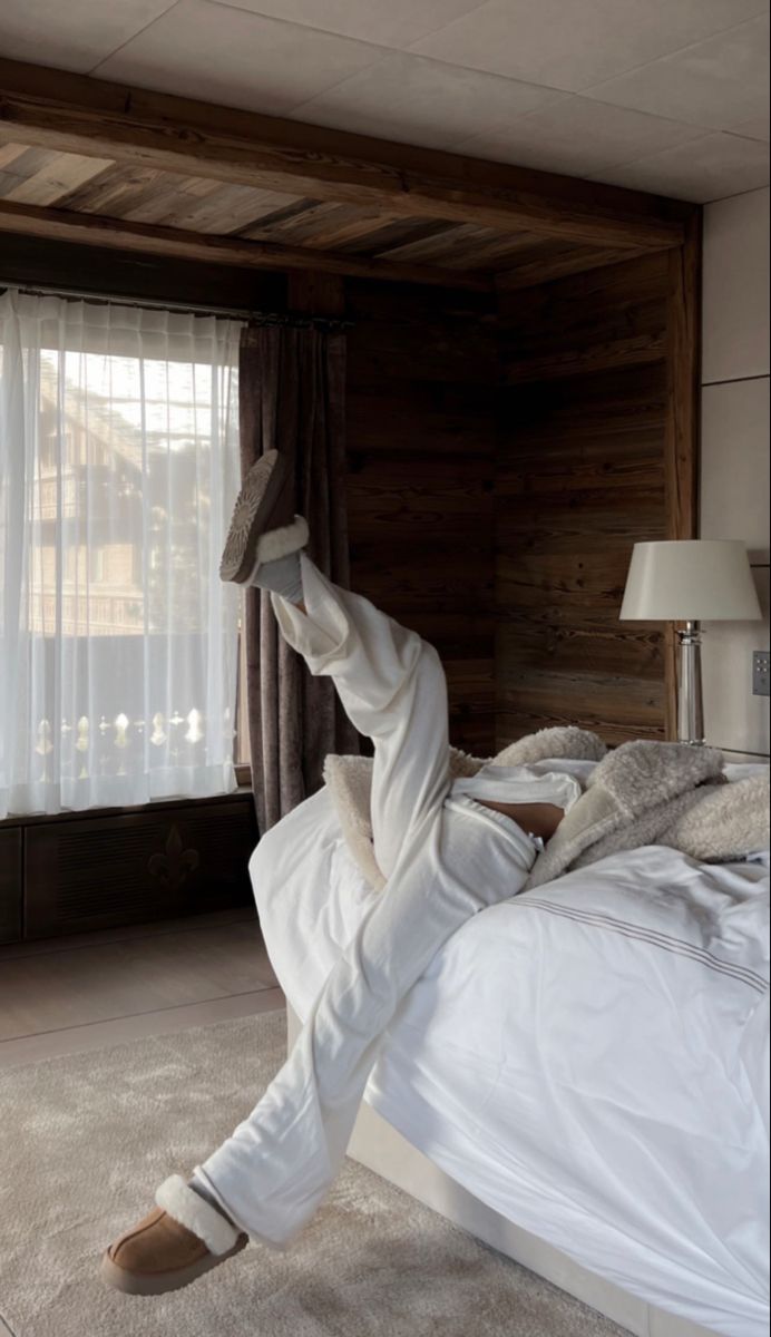 a person laying on top of a bed in a room with wooden walls and windows