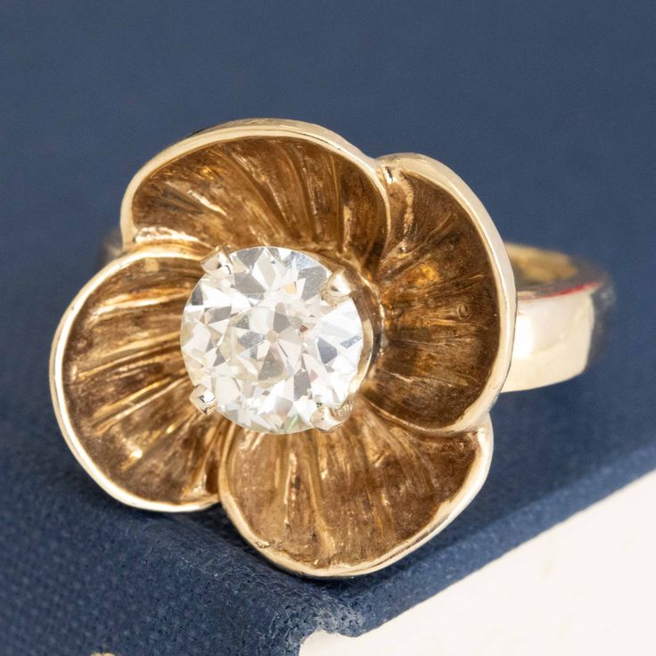 We've grown quite fond of this retro gold floral ring, set with a sparkly and prismatic antique Old European cut diamond in the center! This sweet-as-pie ring has so much charm, from the engraved details of the inner petals to the patina developed throughout. Not to mention that fiery old cut diamond center! 14kt yellow gold Size 6.5 & resizable Diamond is estimated to be N/O color & VS2/SI2 clarity. GIA Standards Please see qualitative report for more information. Video Below Anniversary Jewelry With Rose Cut Diamonds In Flower Shape, Flower-shaped Rose Cut Diamond Jewelry For Anniversary, Flower Shaped Rose Cut Diamond Jewelry For Anniversary, Vintage 14k Gold Flower Ring For Formal Occasions, Fine Jewelry With Flower-shaped Center Stone, Vintage Flower Shaped Jewelry With Rose Cut Diamonds, Vintage Flower Shaped Ring As Gift, Vintage Yellow Gold Flower Wedding Ring, Vintage Diamond Cut Jewelry For Anniversary