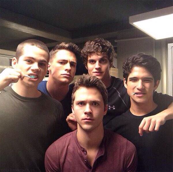 six young men are posing for the camera in front of a bathroom mirror, one is brushing his teeth