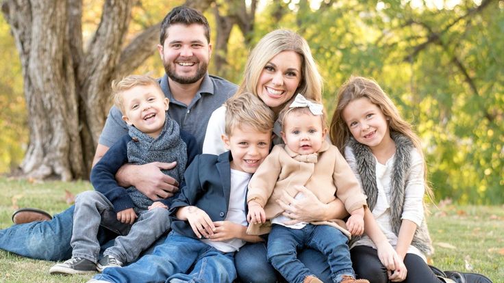 a family sitting on the grass in front of some trees and smiling at the camera