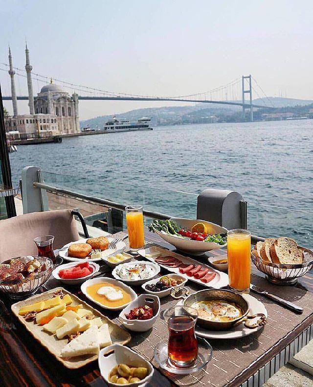 an outdoor dining table with food and drinks on it near the water's edge