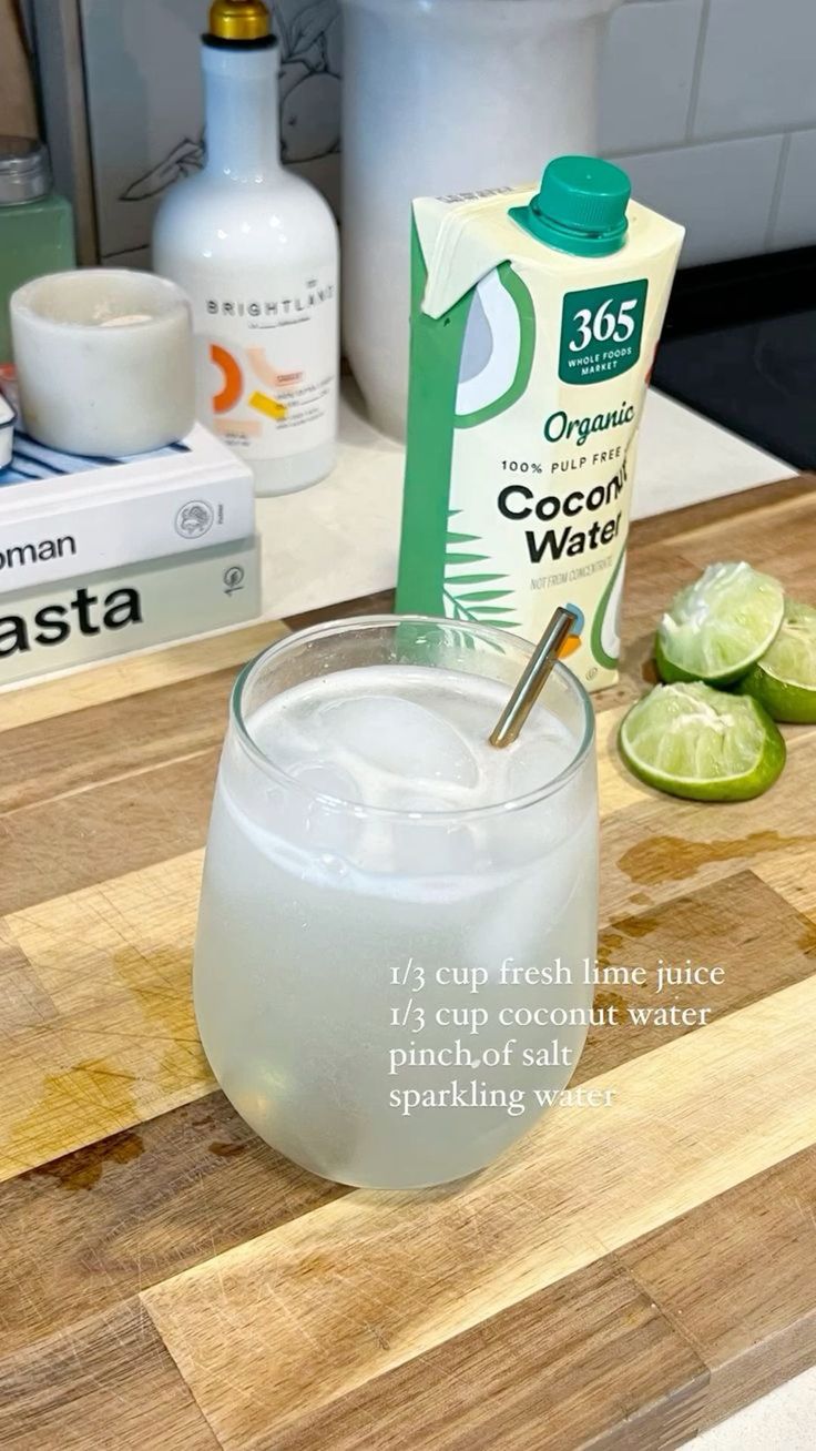 the ingredients to make an alcoholic drink are displayed on a cutting board, including limes and coconut water