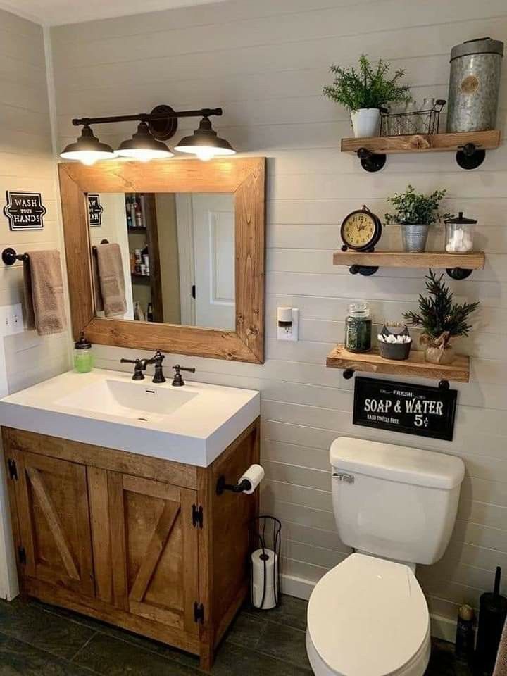 a white toilet sitting under a bathroom mirror next to a wooden sink vanity with open shelving above it