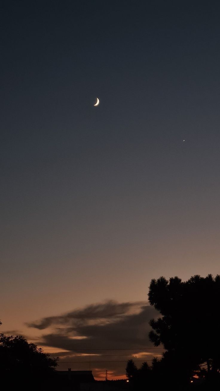 the moon and venus are seen in the sky at dusk, with trees silhouetted against it