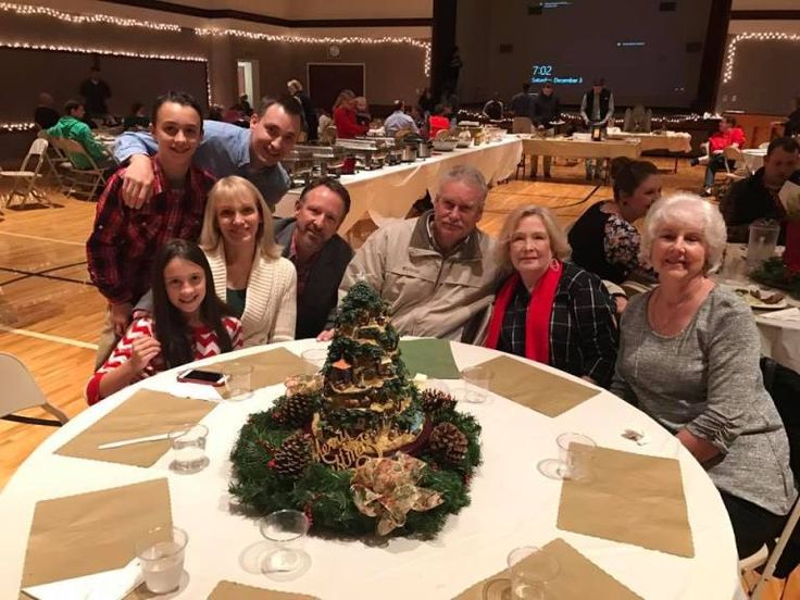 a group of people standing around a table with a christmas tree on top of it