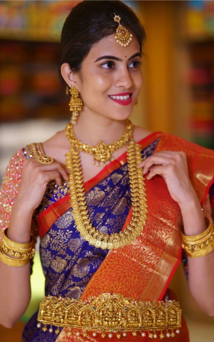 a woman in a blue and orange saree with gold jewelry on her neck, smiling