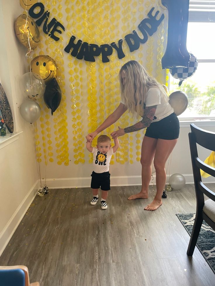 a woman and child standing in front of a birthday backdrop