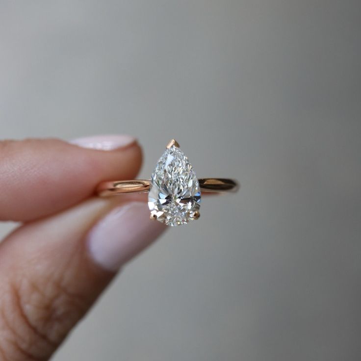 a woman's hand holding an engagement ring with a pear shaped diamond