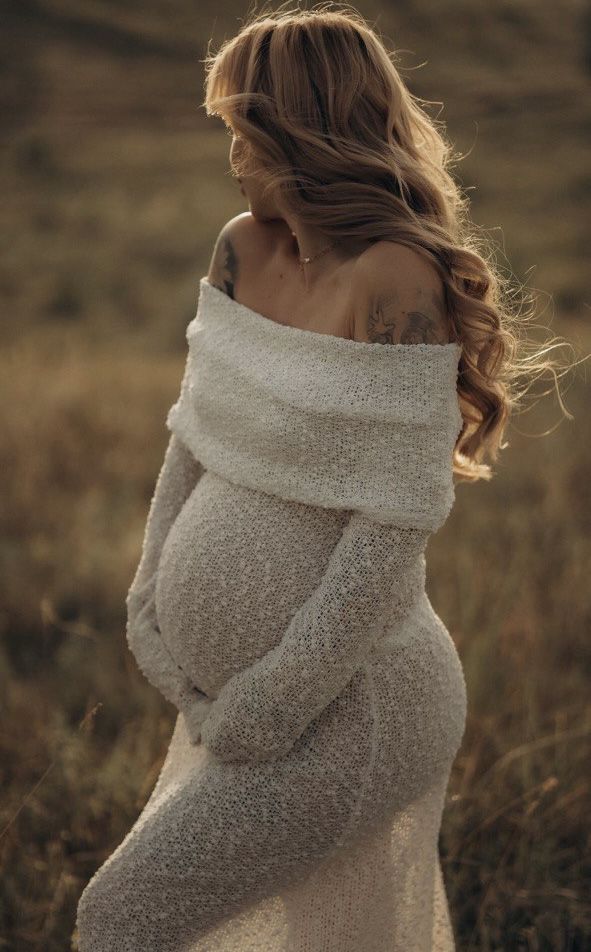 a pregnant woman in a white dress standing in a field