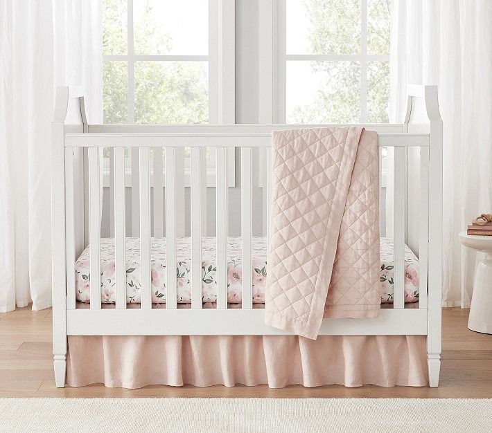 a white crib with pink bedding and curtains