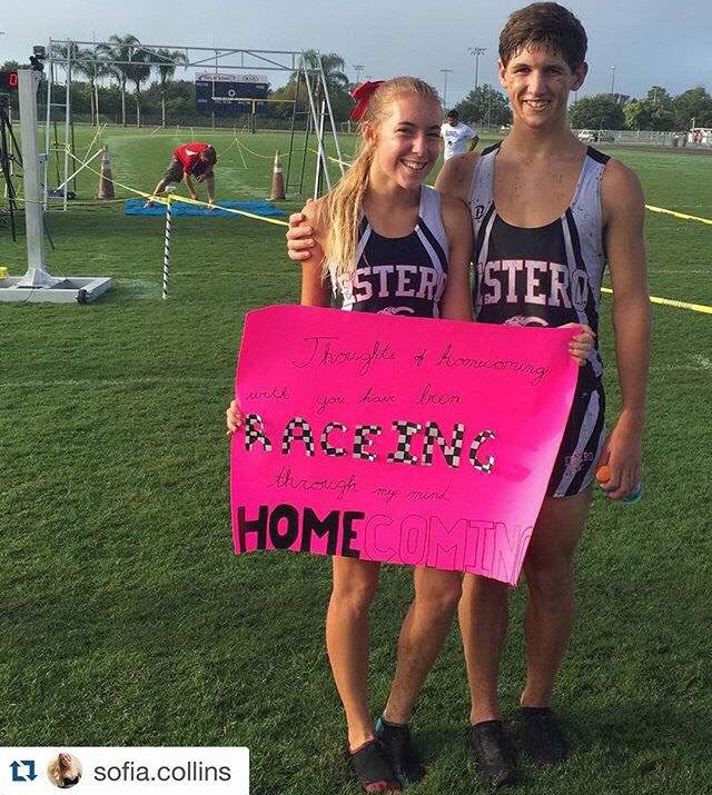 two girls holding up a pink sign in front of a soccer field with other people