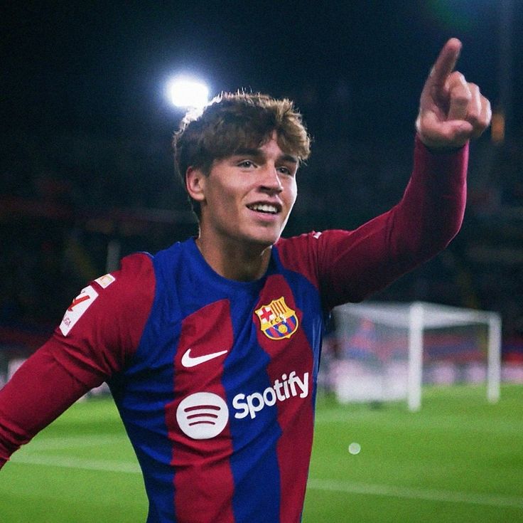 a young man in a red and blue shirt is on the soccer field with his hand up