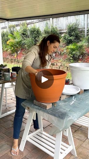 a woman standing over a pot on top of a table next to a white chair