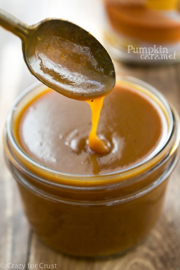 a spoon full of caramel sauce on top of a wooden table with another jar in the background