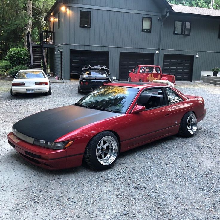 a red sports car parked in front of a garage with two other cars behind it