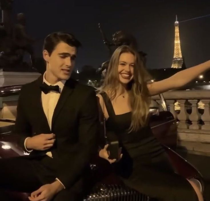 a man and woman sitting on top of a car in front of the eiffel tower