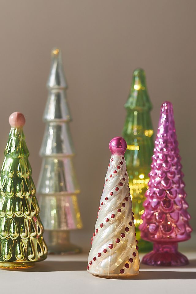 small glass christmas trees are lined up on the counter top in different colors and sizes