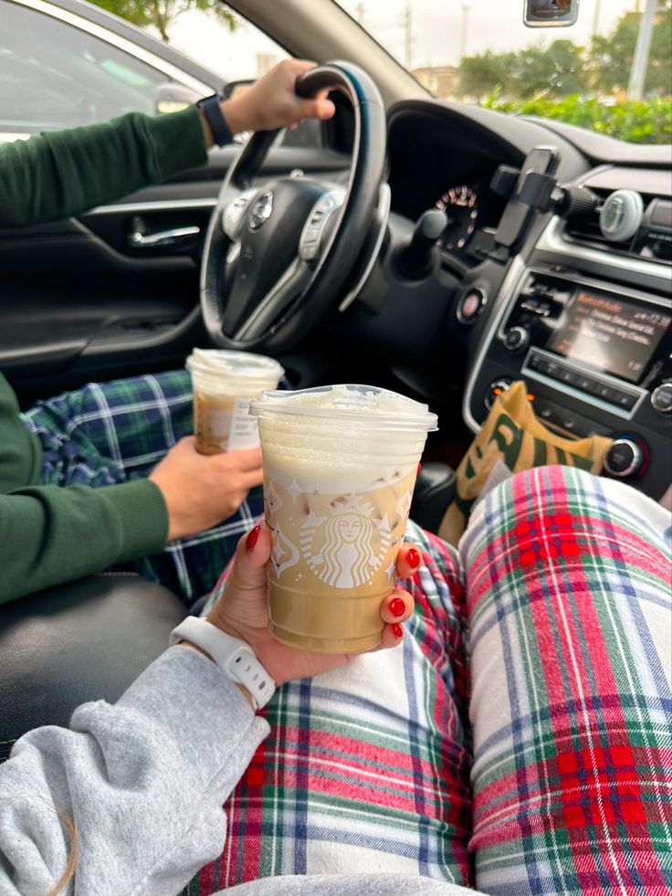 two people sitting in the drivers seat of a car holding cups of coffee