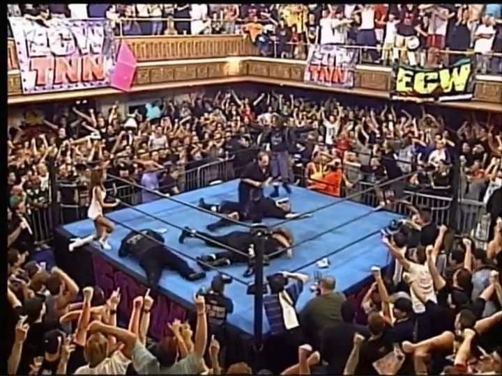 a man standing on top of a blue wrestling ring surrounded by people holding their hands in the air