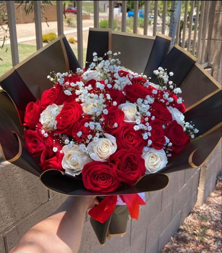 a bouquet of red and white flowers in someone's hand on the side of a building