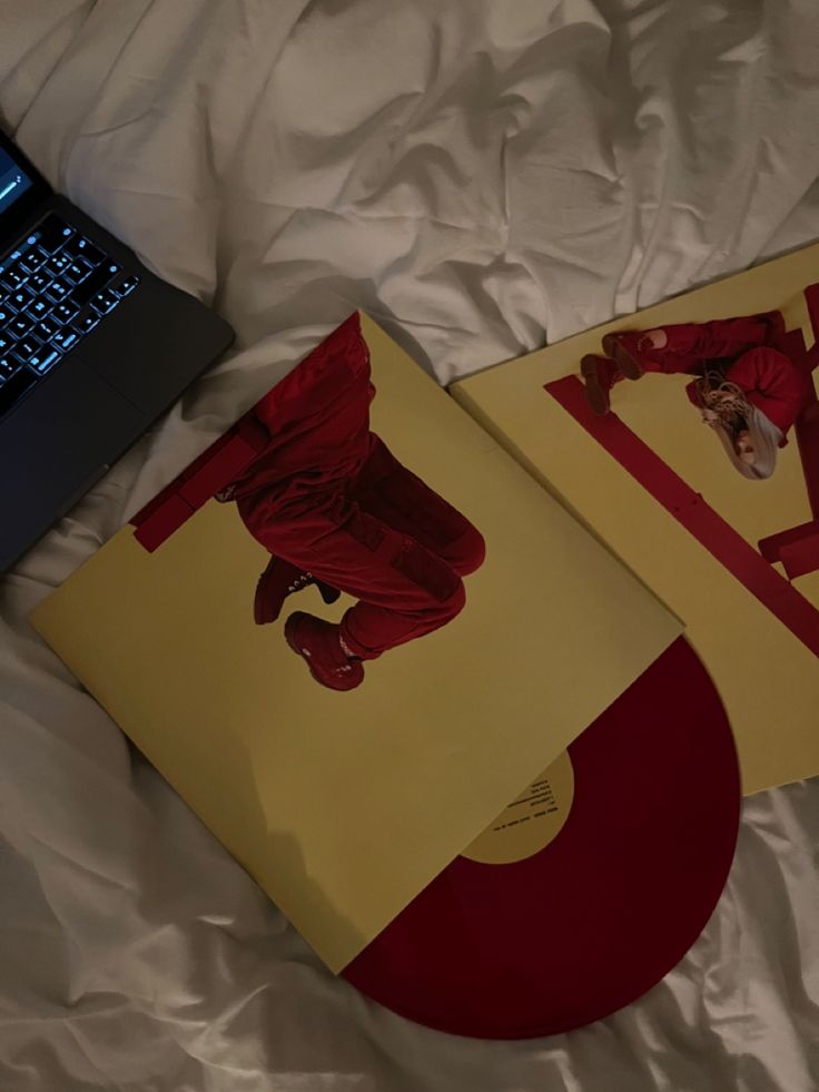 an open laptop computer sitting on top of a bed next to a red and yellow record