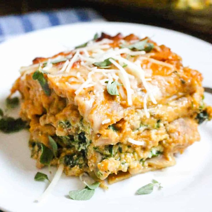 a white plate topped with lasagna covered in cheese and greens on top of a table