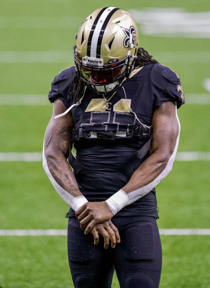 a football player wearing a black and gold uniform on the sidelines with his hands in his pockets