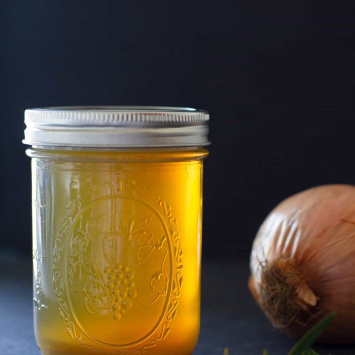 a jar filled with liquid next to garlic and an onion on a counter top,