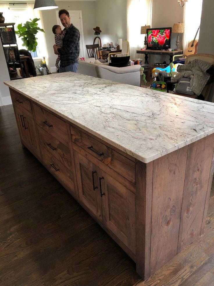 a man standing in the middle of a kitchen with an island made out of wood