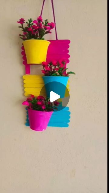 three colorful flower pots hanging on a wall with a video play button below the image