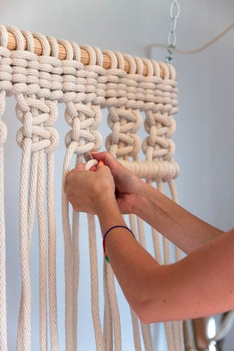 a woman is working on a macrame wall hanging from the ceiling with her hands