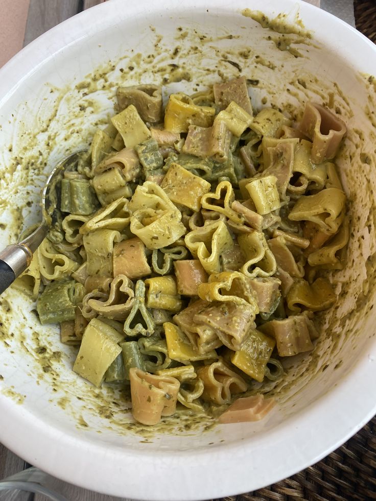 a white bowl filled with pasta and pesto on top of a wicker table