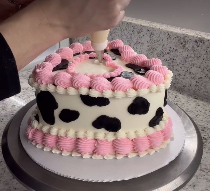 a person is decorating a cake with pink and black icing